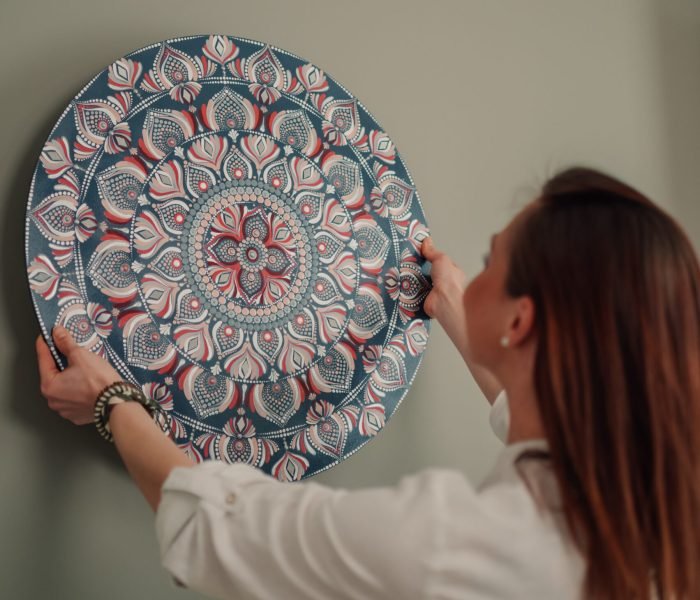 Interior designer hanging a large, round mandala painting on a vibrant green wall, infusing the space with bohemian flair and a sense of spirituality and tranquility
